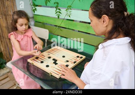 Mutter und Tochter genießen eine gute gemeinsame Zeit beim Spielen von Backgammon in einer ruhigen Umgebung im Freien. Familienbindung, Freizeitaktivitäten und kognitive d Stockfoto