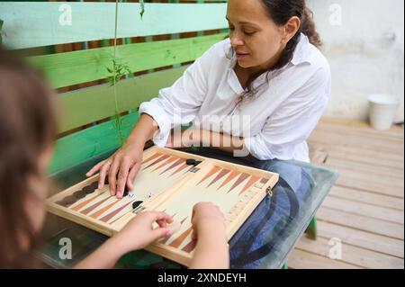 Mutter und Tochter genießen gute Zeit beim Spielen von Backgammon auf einem Holzbrett. Im Freien mit ungezwungener und entspannter Atmosphäre. Stockfoto