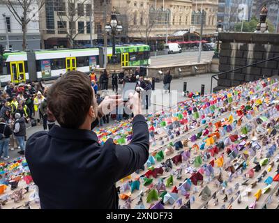 Melbourne, Australien. 31. Juli 2024. Ein Teilnehmer fotografiert das Display von oben. 6.000 Origami-Häuser wurden vom Victorian Homeless Network auf den Stufen des Parlamentsgebäudes von Victoria platziert und symbolisieren 10 % der Sozialwohnungen, die im Staat benötigt werden, um die Obdachlosigkeit zu beenden. Quelle: SOPA Images Limited/Alamy Live News Stockfoto