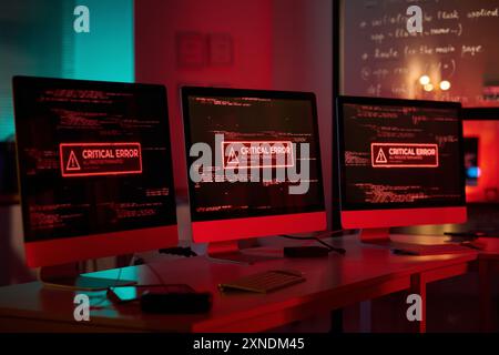 Hintergrundbild von drei Computermonitoren mit Notfallmeldungen auf dem Bildschirm im Kopierraum mit roten Lichtern Stockfoto