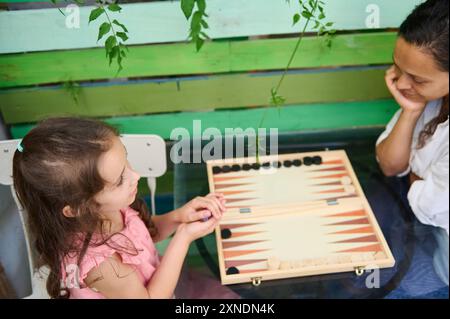 Eine Mutter und Tochter genießen einen Bindungsmoment, während sie zu Hause eine Runde Backgammon spielen. In dieser verspielten, gemütlichen Szene treffen sich Familienzeit und Freizeit. Stockfoto