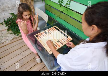 Ein herzerwärmender Moment, in dem Mutter und Tochter gemeinsam Backgammon in einem gemütlichen Garten spielen, um die Bindung und den Spaß der Familie zu fördern. Stockfoto