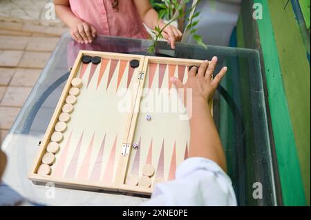 Zwei Personen, die sich auf einem Glastisch mit Backgammon Vergnügen. Konzentrieren Sie sich auf das Brett und würfeln Sie, um eine entspannte und angenehme Atmosphäre zu schaffen. Stockfoto