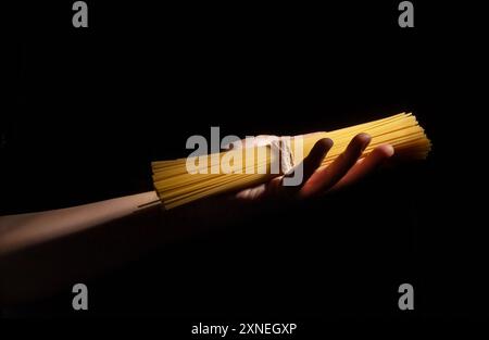 Nudelspaghetti in der Hand auf schwarzem Hintergrund Stockfoto