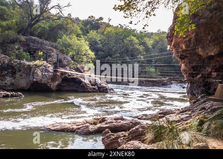 Blick auf einen Hennops Wander Trail, mit Fluss, kleiner Brücke und Seilbahn über den Fluss, Hartbeespoort, Johannesburg, Südafrika Stockfoto