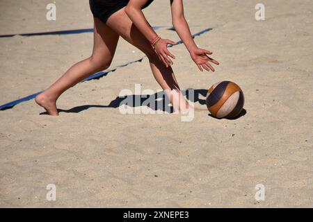 Ein Beachvolleyballspieler sammelt den Ball nach einem stark umstrittenen Punkt während eines Spiels. Stockfoto