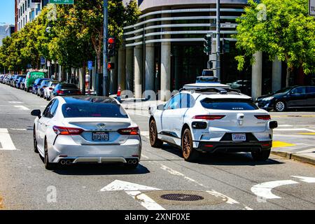 Zwei Fahrzeuge an einer Ampel: Eine weiße Limousine und ein selbstfahrender Waymo Jaguar mit Dachsensoren – San Francisco, Kalifornien, USA – 22. Juni 2024 Stockfoto