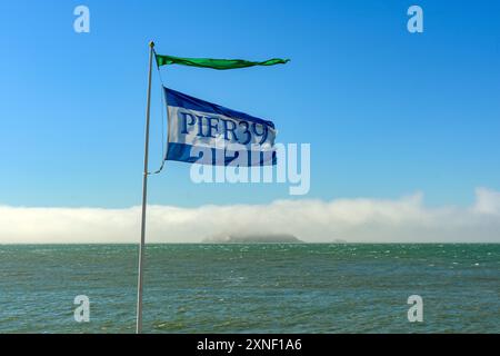 Pier 39 fliegt an Fisherman's Wharf mit der nebligen Alcatraz Island im Hintergrund vor einem klaren blauen Himmel. - San Francisco, Kalifornien, USA - Jun Stockfoto