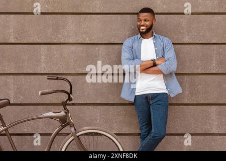 Junger schwarzer Kerl posiert neben dem Fahrrad über der Betonmauer der Stadt Stockfoto