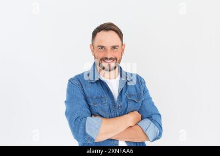 Bild eines glücklichen brünetten Mannes in legeren Kleidern, mit gekreuzten Armen, der mit einem glücklichen, selbstbewussten Lächeln in die Kamera blickt, der vor einem grauen Hintergrund steht Stockfoto