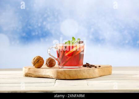 Glühwein in einem Glas mit Zimtschnecken auf einem Holztisch vor dem Hintergrund eines verschwommenen festlichen, schneebedeckten Winterhintergrunds. Ein warmer Getränkekonzept Stockfoto