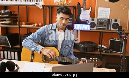 Hübscher hispanischer Mann, der Gitarre spielt in einem Musikstudio mit moderner Aufnahmeausrüstung. Stockfoto