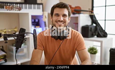 Ein lächelnder hispanischer Mann mit Kopfhörern in einem Musikstudio posiert selbstbewusst. Stockfoto