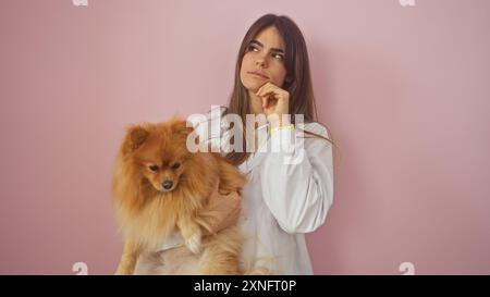 Eine nachdenkliche junge Frau, die einen pommerschen Hund vor einem isolierten rosa Hintergrund hält. Stockfoto