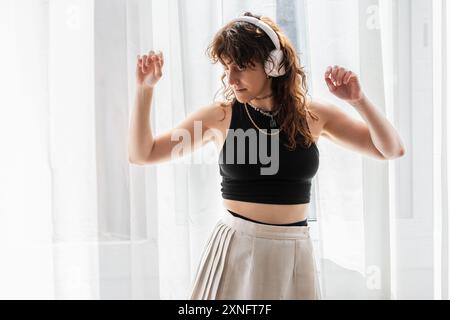 Die Frau tanzt vor dem Fenster, während sie Musik auf ihren Kopfhörern hört. Stockfoto