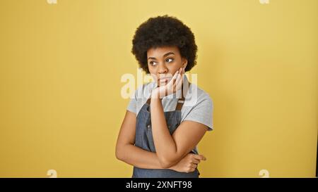 Nachdenkliche afroamerikanische Frau mit lockigen Haaren posiert vor gelbem Hintergrund und zeigt lässige Schönheit. Stockfoto