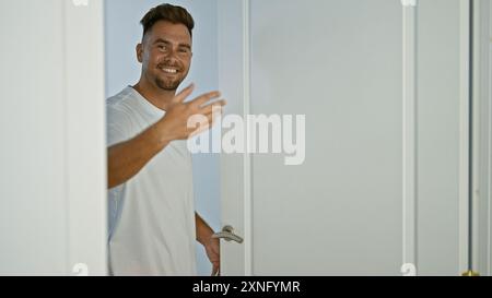 Lächelnder junger Mann mit Bartgrüß von einer Tür in einem modernen Innenraum Stockfoto