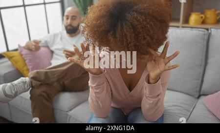 Eine verärgerte Frau gibt Frustration während eines Streits mit einem Mann, der auf einer Couch in einem modernen Wohnzimmer sitzt. Stockfoto