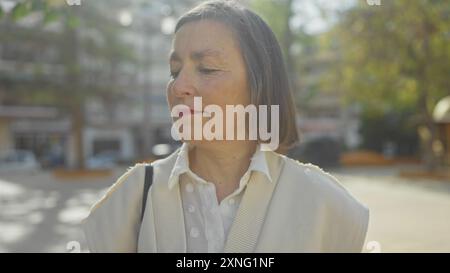 Eine besinnliche Frau mittleren Alters mit kurzen Haaren steht in einem urbanen Park und weckt ein Gefühl der friedlichen Einsamkeit. Stockfoto