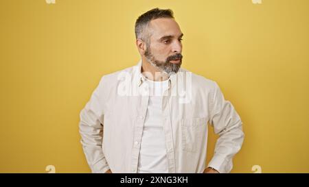 Gutaussehender ranghanischer Mann mit grauem Bart in lässiger Kleidung posiert nachdenklich vor gelbem Hintergrund. Stockfoto