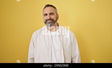 Ein gutaussehender ranghanischer Mann mit Bart und grauen Haaren, der sich vor einem isolierten gelben Hintergrund posiert Stockfoto