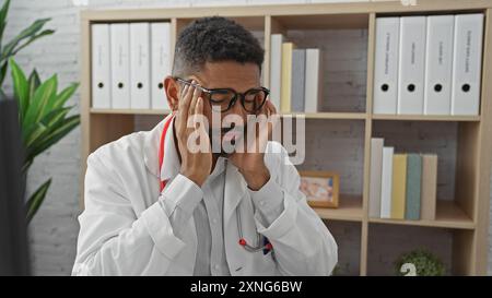 Ein gestresster afroamerikanischer Arzt mit Bart, der in einem Krankenhauszimmer steht. Stockfoto