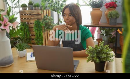 afroamerikanerin Floristin mit Laptop in einem Blumenladen mit Pflanzen, die nachdenklich aussieht. Stockfoto