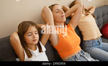 Eine junge Frau und zwei Mädchen entspannen sich mit geschlossenen Augen auf einem grauen Sofa und zeigen einen ruhigen Familienmoment drinnen. Stockfoto