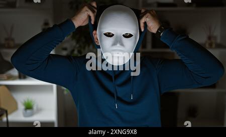 Ein junger Mann in einem Büro, der eine weiße Maske trägt, verschleiert seine Identität und schafft ein Gefühl von Geheimnissen und Anonymität. Stockfoto