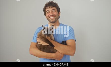 Ein lächelnder junger Mann hält eine siamesische Katze vor einem isolierten weißen Hintergrund. Stockfoto