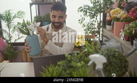Ein junger hispanischer Mann mit Bart arrangiert Blumen in einer Vase während eines Videoanrufs in einem Blumenladen. Stockfoto