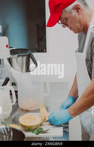 Der Küchenchef mit blauen Handschuhen schneidet in einer kommerziellen Küche eine frische, saftige Melone auf einem Schneidebrett, die wahrscheinlich einen köstlichen Sommergenuss zaubert Stockfoto