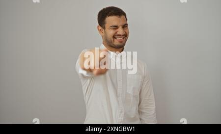 Hübscher junger hispanischer Mann in weißem Hemd, der mit Zwinkern über isolierten weißen Hintergrund zeigt und lächelt Stockfoto