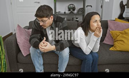 Ein besinnlicher Mann und eine Frau sitzen in einem modernen Wohnzimmer distanziert auf einem Sofa, was eine emotionale Trennung widerspiegelt. Stockfoto