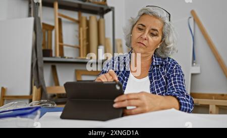 Reife Frau mit Tablet in einer Holzwerkstatt, die Kreativität und technologische Integration demonstriert. Stockfoto