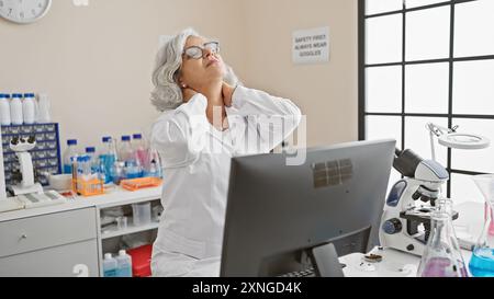 Reife Wissenschaftlerin mit grauen Haaren, die Nackenschmerzen im Labor erlebt. Stockfoto