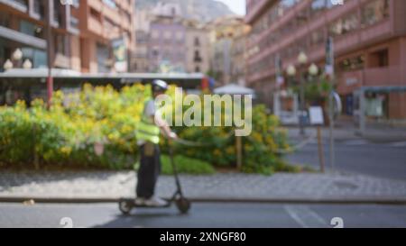 Mann, der auf einem Roller mit Helm und Sicherheitsweste auf der Stadtstraße mit verschwommenem urbanem Hintergrund, Blumen und Gebäuden im Fokus steht Stockfoto