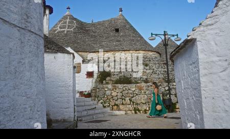 Eine junge hispanische Frau in grünem Kleid schlendert durch die bezaubernden Straßen der Altstadt von alberobello, italien, umgeben von traditionellen Trulli h Stockfoto