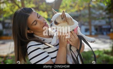 Eine junge hispanische Frau hält liebevoll einen chihuahua im Freien in einem Stadtpark. Stockfoto