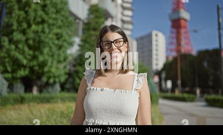 Die lebendige hispanische Frau, die vor Freude strahlt, posiert in einer Brille an tokios berühmtem Stadtviertel und verbreitet ein ansteckendes Lächeln und eine unbeschwerte, selbstbewusste Aura Stockfoto