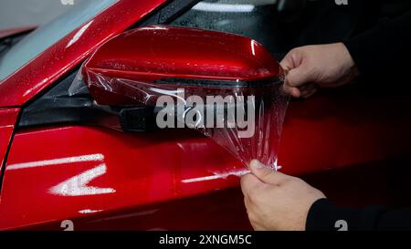 Der Master trägt Vinylfolie auf den Seitenspiegel eines Autos auf. Stockfoto