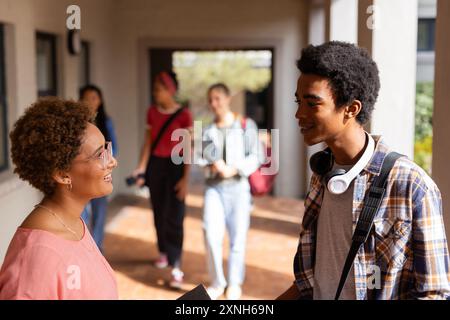 Lehrer und Schüler sprechen im Flur der Highschool, andere Schüler gehen im Hintergrund Stockfoto