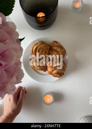 Gemütliche Fika-Einrichtung mit Zimtbrötchen und Kerzen. Perfekt für gemütliche, skandinavische Lifestyle und süße Leckereien. Stockfoto