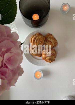 Gemütliche Fika-Einrichtung mit Zimtbrötchen und Kerzen. Perfekt für gemütliche, skandinavische Lifestyle und süße Leckereien. Stockfoto