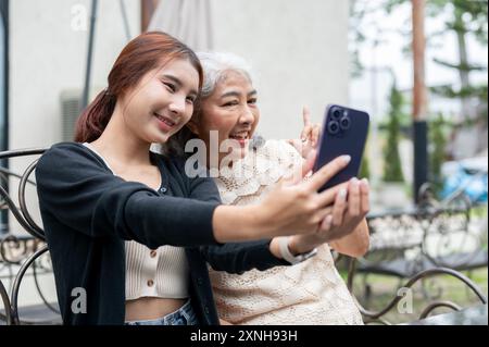 Eine fröhliche junge asiatische Enkelin macht ein Selfie mit ihrer Oma, während sie sich gemeinsam im Garten entspannen, sich um ihre Oma kümmern und Zeit verbringen Stockfoto