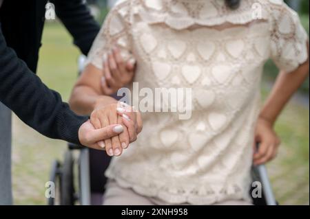 Ein Nahaufnahme-Bild einer fürsorglichen Enkelin, die die Hand ihrer Großmutter hält und ihr hilft, aus dem Rollstuhl aufzustehen und in einem Park zu laufen. Gesundheit, Pflege Stockfoto