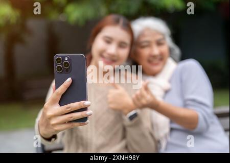 Eine schöne asiatische Enkelin und eine glückliche Oma machen zusammen ein Selfie, während sie sich auf einer Bank im Park ausruhen. Menschen- und Technologiekonzepte. auswahl Stockfoto