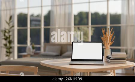 Ein Nahbild eines minimalen Holztisches mit einem Laptop mit einem Mockup auf weißem Bildschirm, Büchern und einer Vase in einem modernen skandinavischen Be Stockfoto
