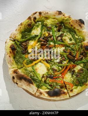 Herzhafte Pizza mit lebhaftem Gemüse, cremigem Käse und einem Hauch Pesto Stockfoto