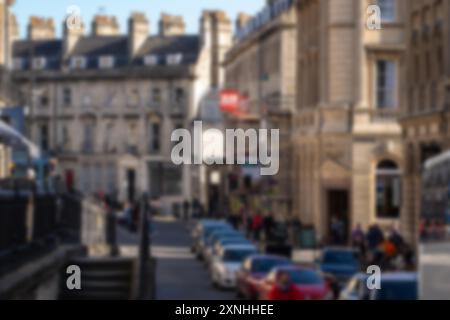 Verschwommener Blick auf eine Straße in Bath, Großbritannien, mit historischen Gebäuden, Menschen zu Fuß und Autos, die entlang der Straße geparkt sind. Stockfoto
